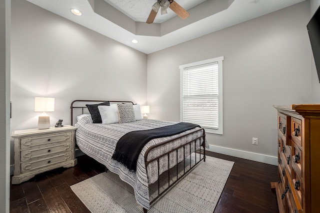 bedroom with a raised ceiling, dark hardwood / wood-style floors, and ceiling fan