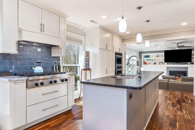 kitchen with crown molding, white cabinetry, a center island with sink, dark hardwood / wood-style flooring, and decorative light fixtures