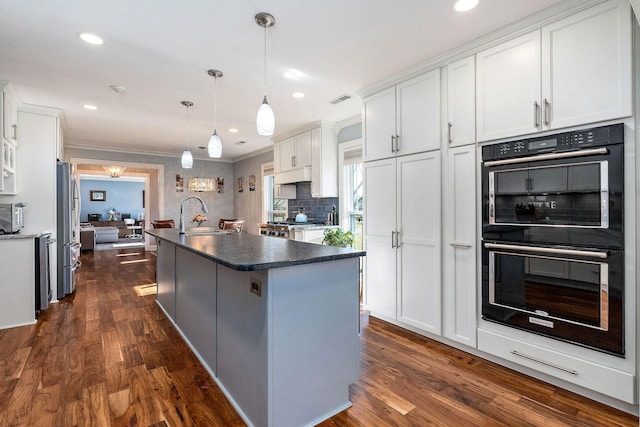 kitchen with a center island with sink, double oven, pendant lighting, decorative backsplash, and white cabinets