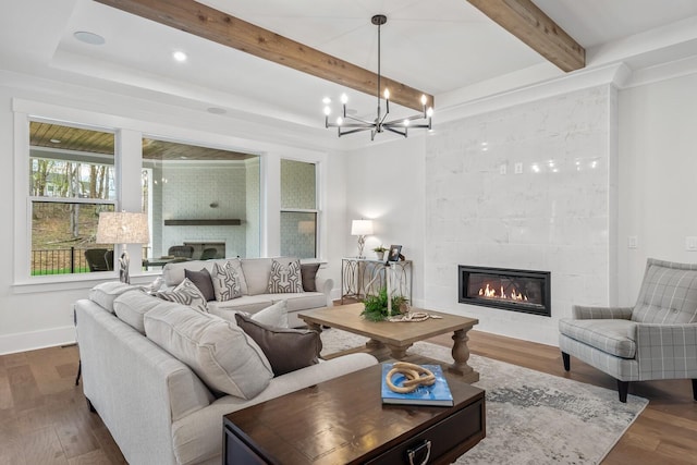 living room with a tiled fireplace, an inviting chandelier, dark hardwood / wood-style flooring, and beam ceiling