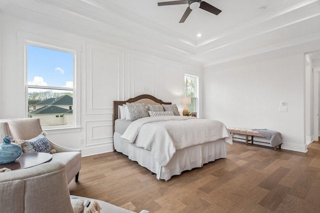 bedroom featuring multiple windows, hardwood / wood-style flooring, a tray ceiling, and ceiling fan