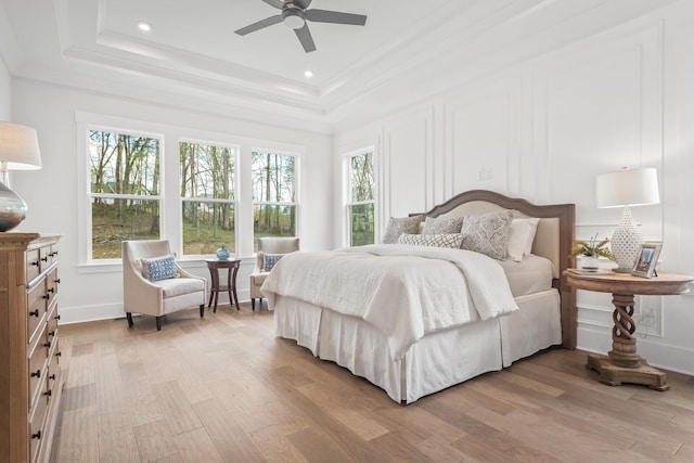 bedroom with light wood-type flooring, ceiling fan, and a tray ceiling