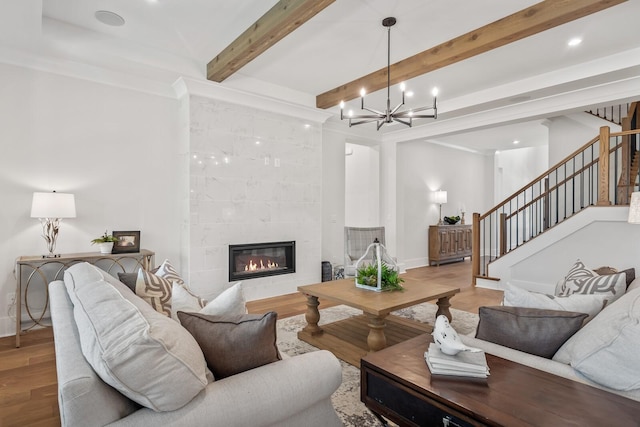 living room featuring ornamental molding, a tile fireplace, a notable chandelier, beam ceiling, and hardwood / wood-style floors