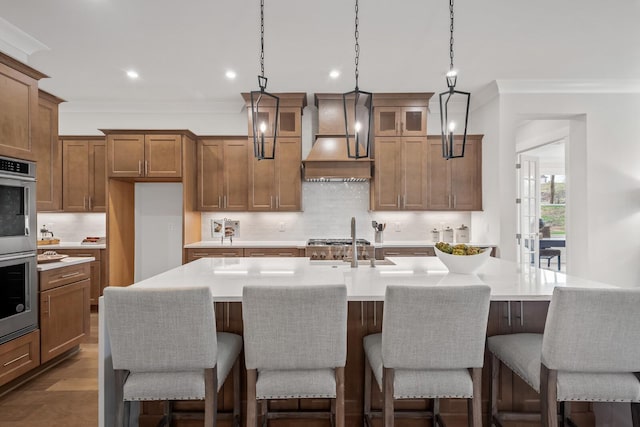 kitchen featuring premium range hood, ornamental molding, an island with sink, and a breakfast bar area