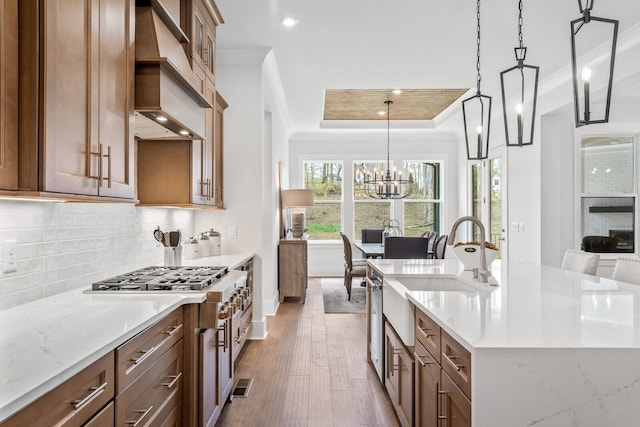 kitchen featuring custom exhaust hood, decorative light fixtures, a raised ceiling, a notable chandelier, and hardwood / wood-style floors