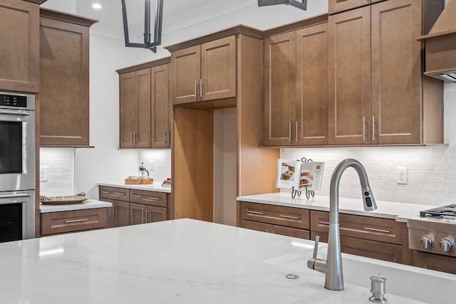 kitchen with double oven, backsplash, decorative light fixtures, and light stone countertops