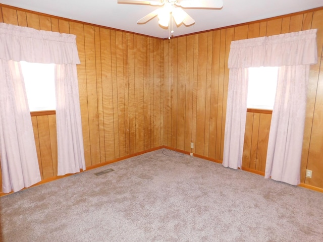 carpeted spare room with crown molding, ceiling fan, and wood walls