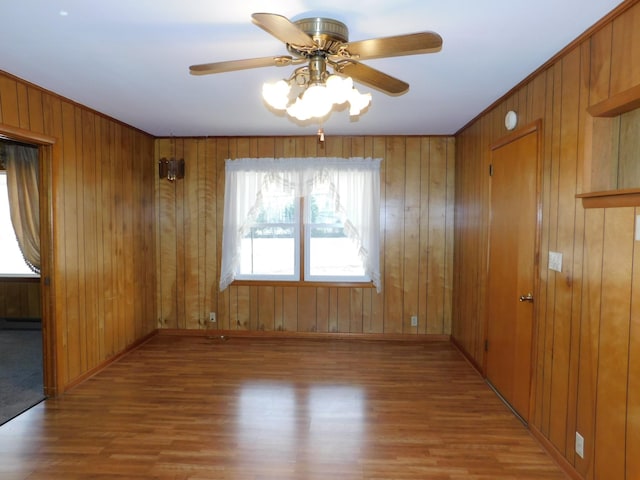 unfurnished room with hardwood / wood-style flooring, ceiling fan, and wood walls