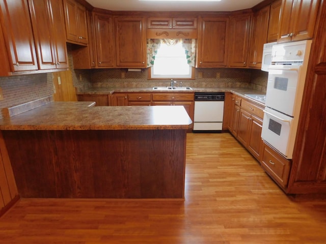 kitchen with sink, tasteful backsplash, light wood-type flooring, kitchen peninsula, and white appliances