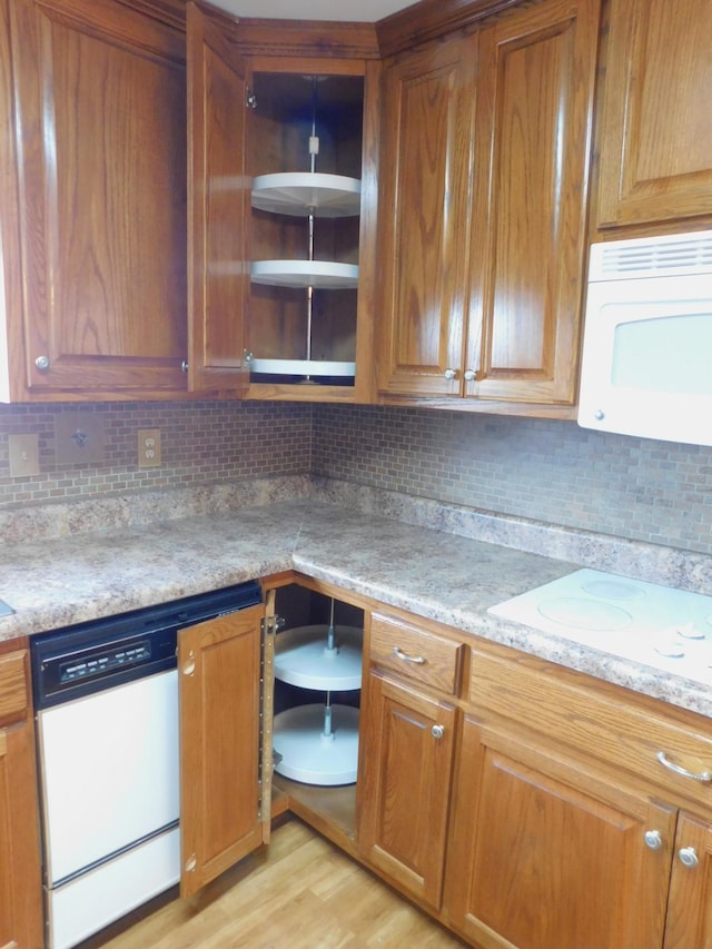 kitchen with tasteful backsplash, light stone counters, white appliances, and light hardwood / wood-style flooring