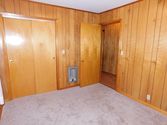 unfurnished bedroom featuring crown molding, wooden walls, heating unit, light colored carpet, and a closet