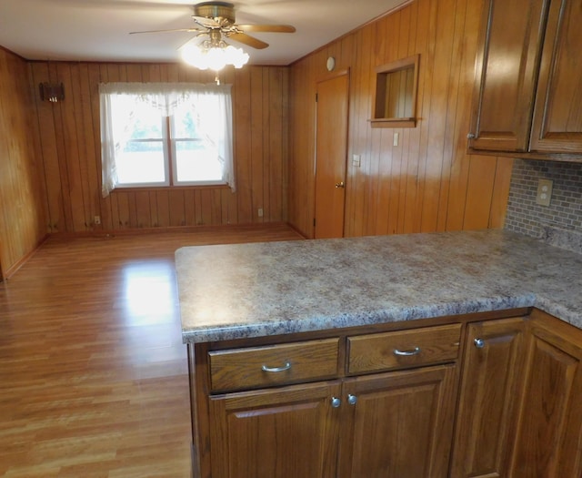 kitchen with wooden walls, light stone counters, ceiling fan, and light hardwood / wood-style flooring