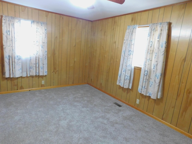 spare room featuring carpet flooring, wooden walls, and ceiling fan