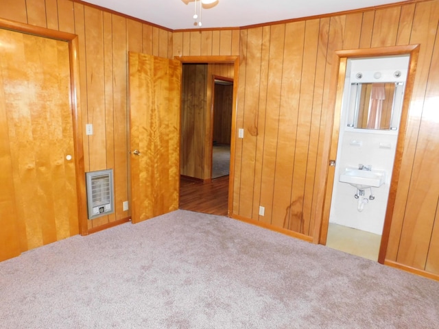 unfurnished bedroom with heating unit, wood walls, sink, carpet flooring, and crown molding