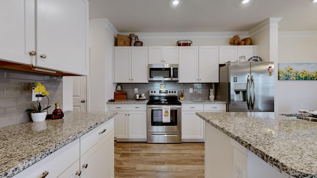 kitchen featuring tasteful backsplash, appliances with stainless steel finishes, light hardwood / wood-style flooring, and white cabinets