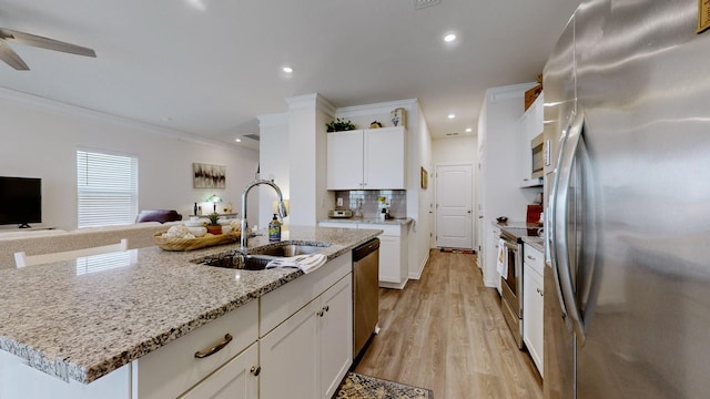 kitchen with sink, appliances with stainless steel finishes, white cabinetry, light stone countertops, and a center island with sink