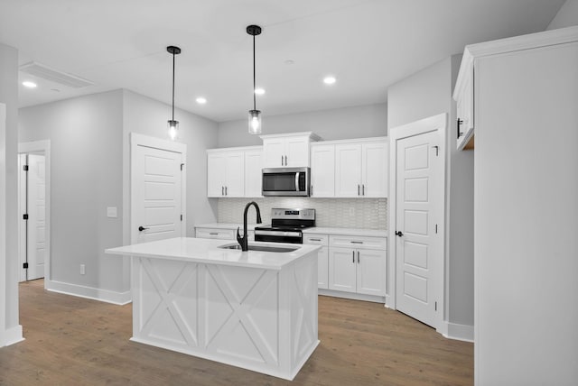 kitchen featuring appliances with stainless steel finishes, decorative light fixtures, sink, white cabinets, and a center island with sink