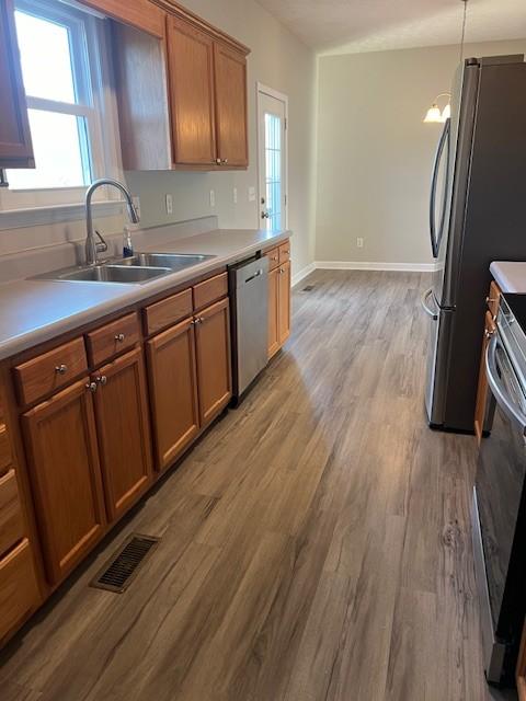 kitchen with sink, decorative light fixtures, stainless steel appliances, and light wood-type flooring