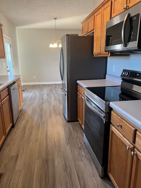 kitchen featuring stainless steel appliances, wood-type flooring, a chandelier, and decorative light fixtures