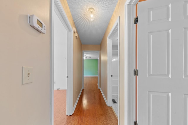 corridor with light wood-type flooring and a textured ceiling