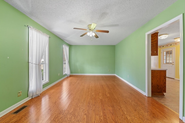 empty room with a textured ceiling, ceiling fan, and light wood-type flooring