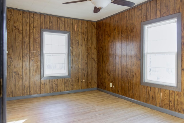 unfurnished room featuring ceiling fan, wooden walls, light hardwood / wood-style flooring, and a wealth of natural light