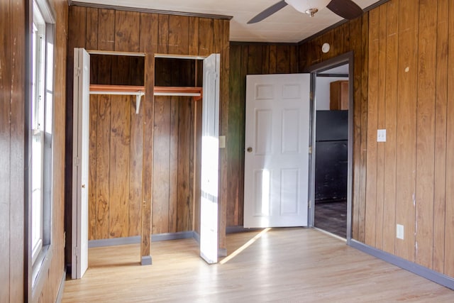 unfurnished bedroom featuring light hardwood / wood-style flooring, ceiling fan, wooden walls, black fridge, and a closet