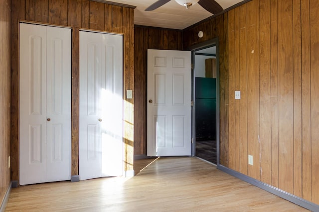 unfurnished bedroom with two closets, light wood-type flooring, ceiling fan, and wood walls