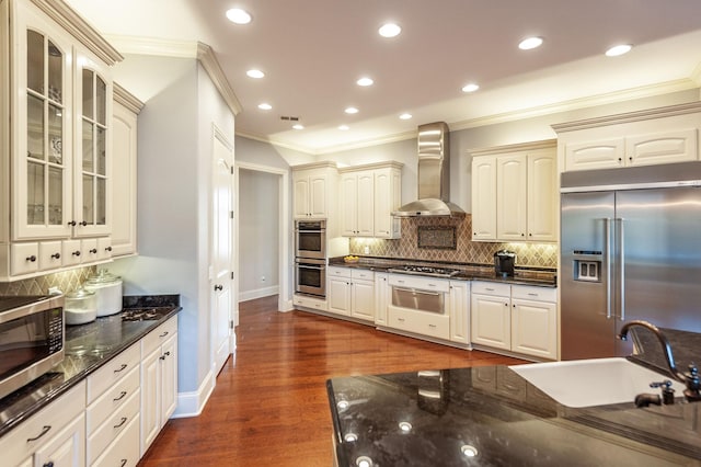 kitchen featuring appliances with stainless steel finishes, dark hardwood / wood-style floors, sink, dark stone counters, and wall chimney range hood