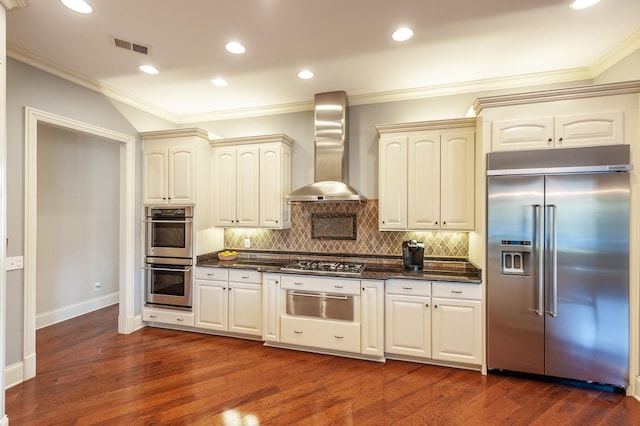 kitchen featuring stainless steel appliances, dark hardwood / wood-style flooring, decorative backsplash, dark stone counters, and wall chimney exhaust hood