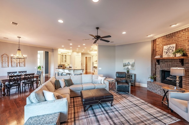 living room with dark wood-type flooring, a fireplace, crown molding, and ceiling fan with notable chandelier