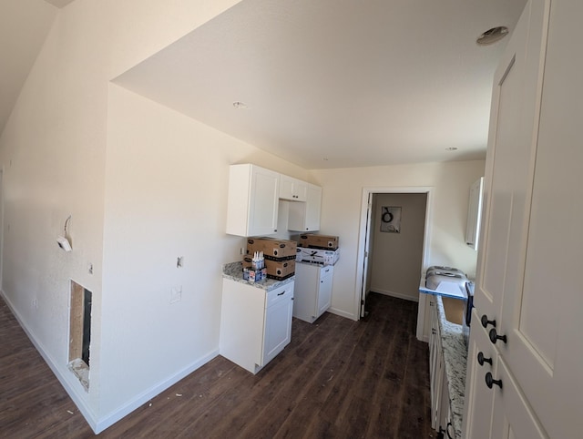 kitchen with light stone counters, dark wood finished floors, white cabinetry, and baseboards