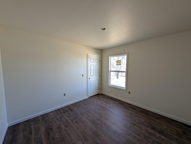 spare room with baseboards and dark wood-style flooring