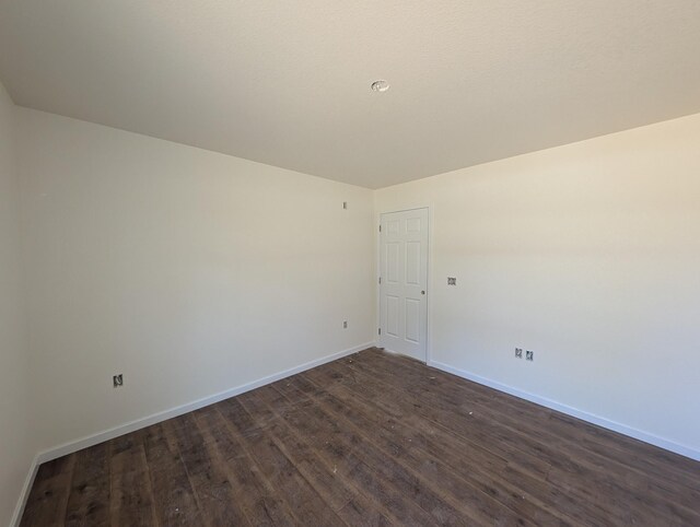 spare room featuring dark wood-type flooring and baseboards