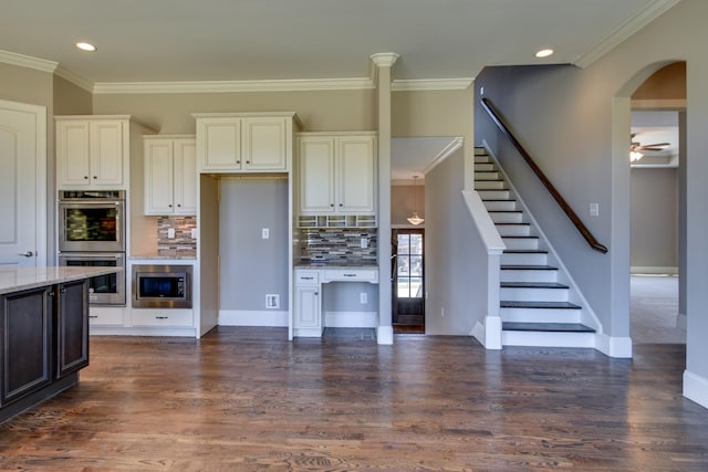 kitchen featuring light stone counters, ornamental molding, appliances with stainless steel finishes, decorative backsplash, and white cabinets