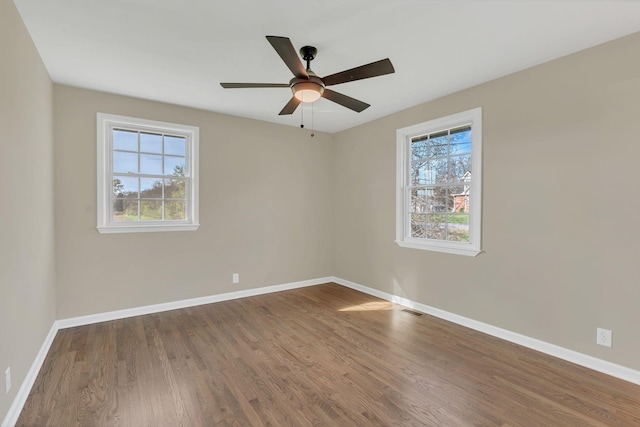 empty room with ceiling fan, a healthy amount of sunlight, and dark hardwood / wood-style flooring