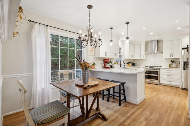 kitchen with hanging light fixtures, wall chimney range hood, kitchen peninsula, stainless steel appliances, and white cabinets