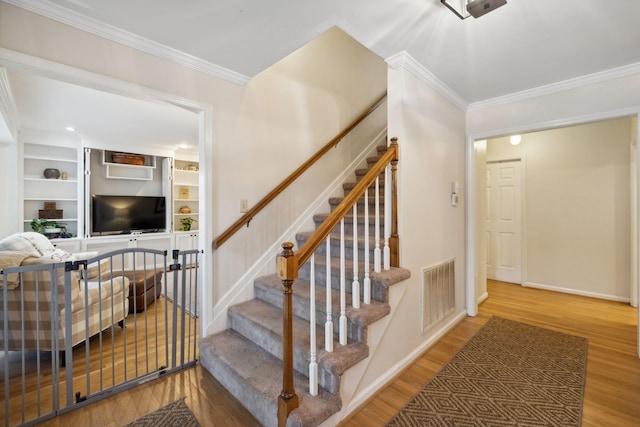 stairs featuring ornamental molding, wood-type flooring, and built in features