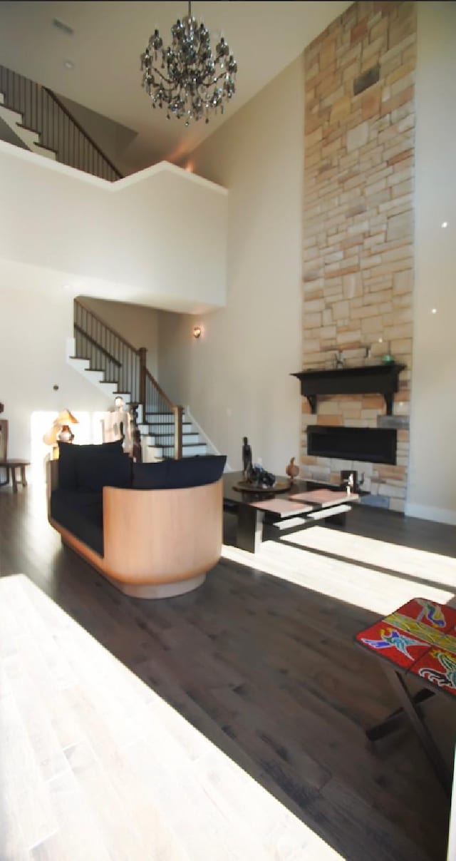 interior space featuring hardwood / wood-style floors, a stone fireplace, a chandelier, and a high ceiling