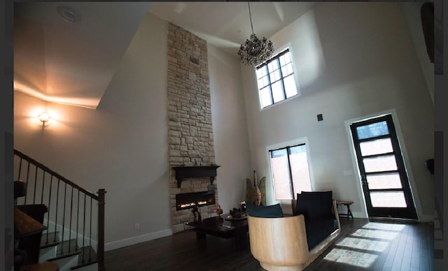 living room with dark wood-type flooring, a towering ceiling, a fireplace, and a notable chandelier