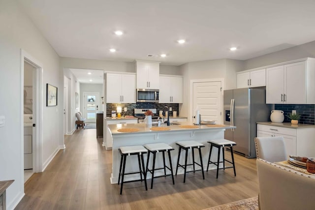 kitchen featuring white cabinetry, a kitchen island with sink, stainless steel appliances, and a kitchen bar