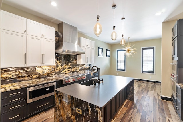 kitchen with pendant lighting, sink, a kitchen island with sink, white cabinetry, and ventilation hood