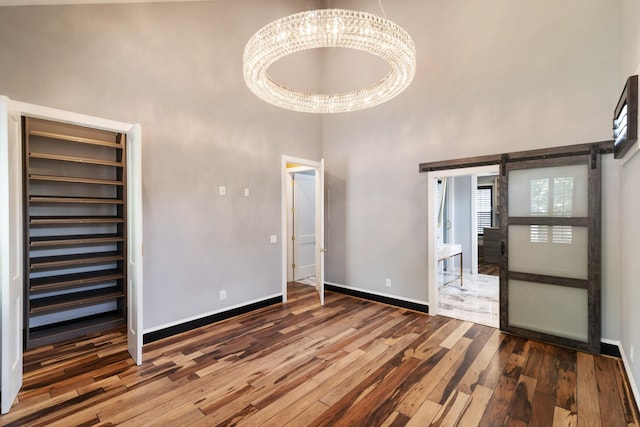 unfurnished bedroom featuring a notable chandelier, a towering ceiling, wood-type flooring, and a barn door