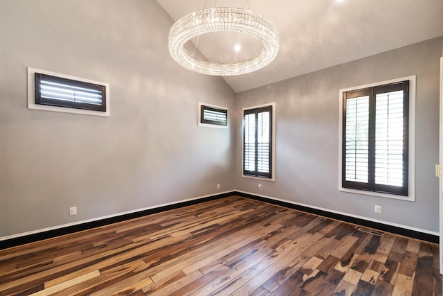 spare room featuring vaulted ceiling, a healthy amount of sunlight, and hardwood / wood-style floors