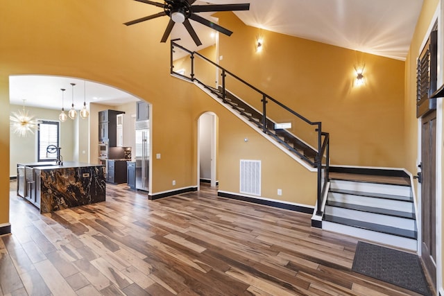 living room featuring dark wood-type flooring, ceiling fan with notable chandelier, and a towering ceiling