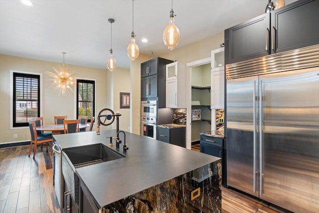 kitchen featuring appliances with stainless steel finishes, wood-type flooring, hanging light fixtures, and a center island with sink