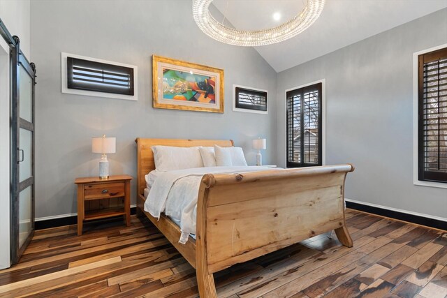 bedroom featuring lofted ceiling, a barn door, and dark hardwood / wood-style flooring