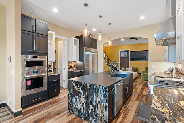 kitchen with a kitchen island with sink, stainless steel appliances, light hardwood / wood-style floors, island exhaust hood, and decorative light fixtures