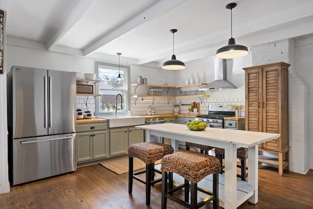 kitchen featuring appliances with stainless steel finishes, decorative light fixtures, backsplash, green cabinetry, and wall chimney exhaust hood