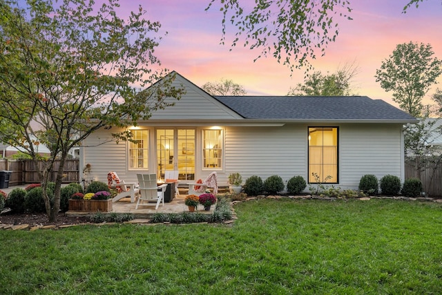 back house at dusk with a patio and a lawn